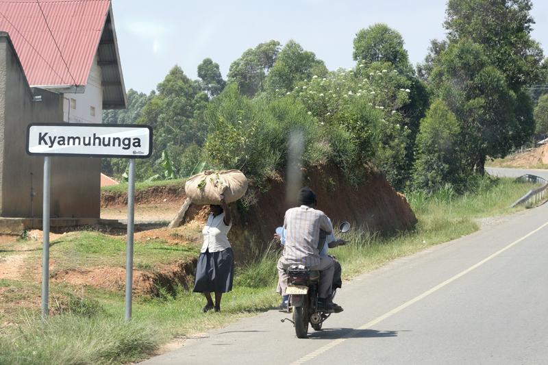 Kyamuhunga town sign, person on a motorcycle and person carrying a bundle on their head, Uganda