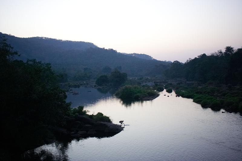 Silhouette of a man washing clothes at dusk, near Vazhachal Falls, Ernakulam, Kerala, India