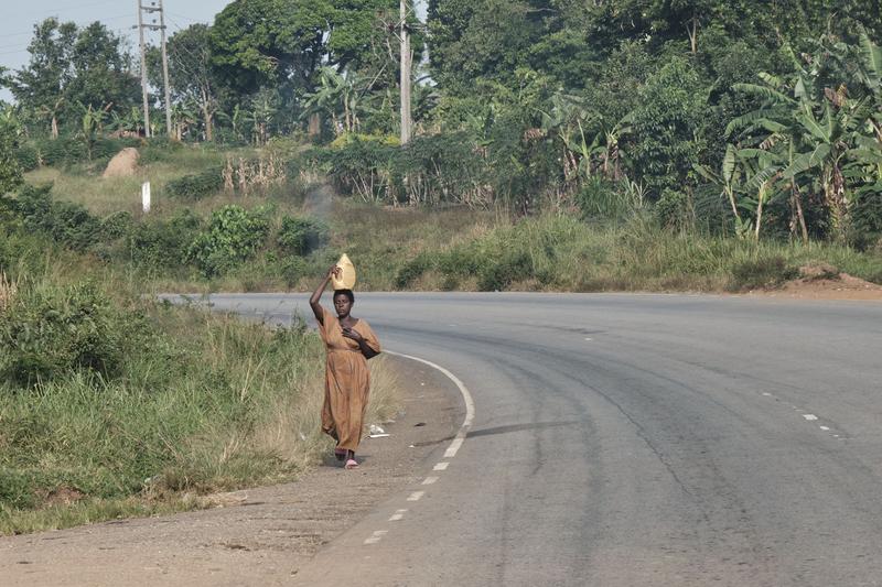 Woman walking down the street while balancing a water jug on her head, Entebbe, Uganda