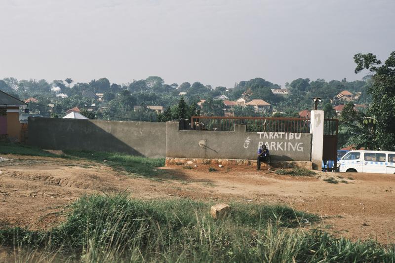 Person sitting on a curb under a parking sign, Uganda