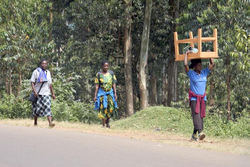 People walking along the street, one person is carrying a table on their head, Uganda