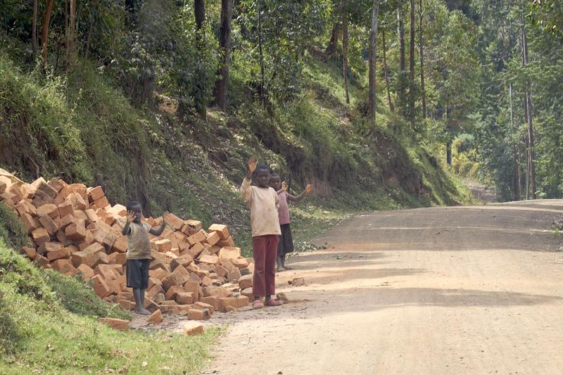 Three kids waving with their hands covered in brick dust, Uganda